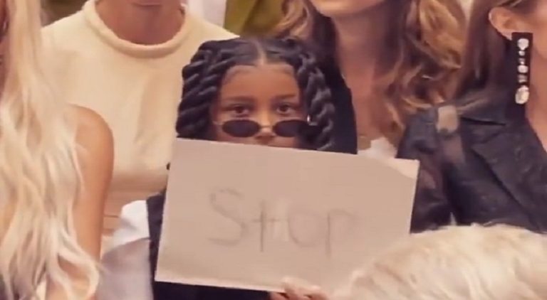 North West holds up sign that reads STOP to people taking pictures of her