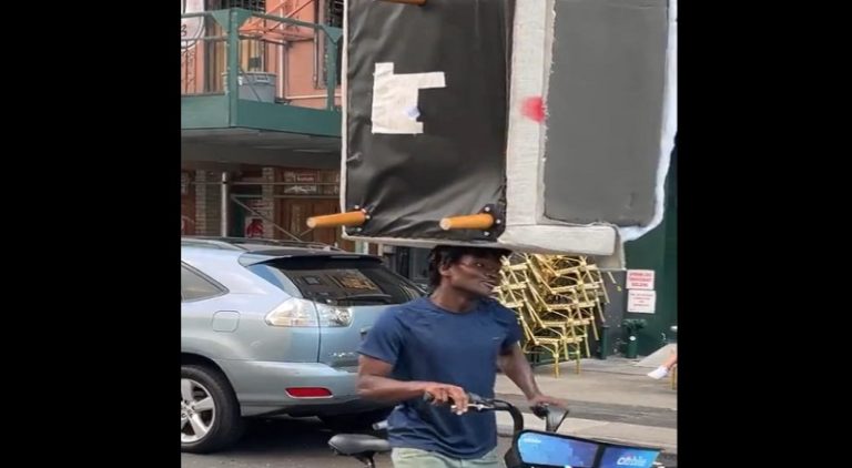 Man balances couch on his head while riding bike
