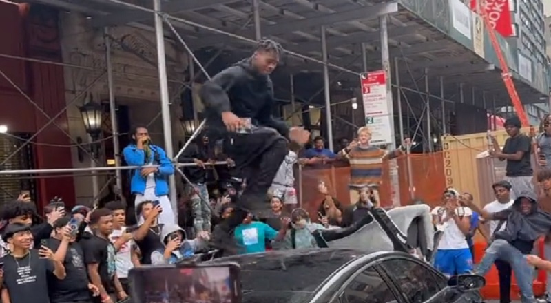 People in NYC destroy a car as one man dances on top of it